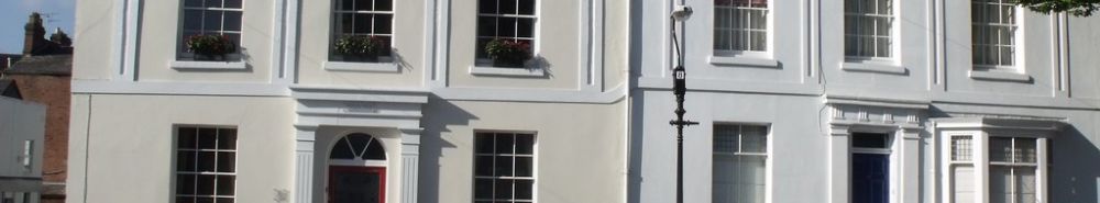 A white-painted terrace with an arched doorway, red front door and window boxes in flower.