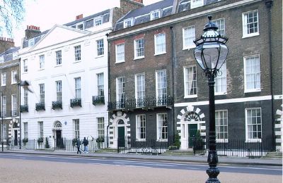 A pair of stucco-fronted and brick townhouses on a London square, with a cast-iron street lamp in the foreground.