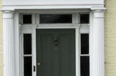 A painted timber front door in a columned porch, with fanlight and side windows above.